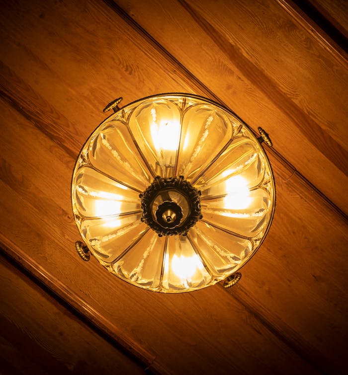 Close-up of an ornate chandelier illuminating a wooden ceiling with warm light.